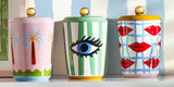 Three colorful jars with decorative designs on a shelf against a striped wall.