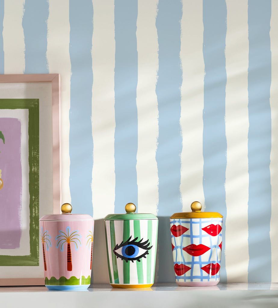 Three colorful jars with decorative designs on a shelf against a striped wall.
